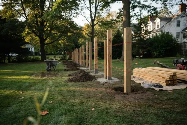 Fence installation in progress: post holes, posts in wet concrete, string line and stacked cedar boards